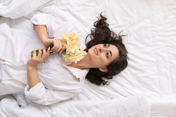 Mujer joven con hermoso ramo de flores narcisas acostado en la cama - Foto, Imagen