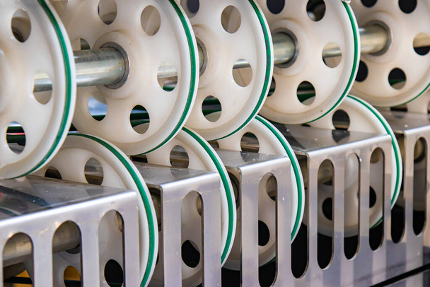 Часть промышленного станка на заводе. Много круглых пластиковых колес для вытягивания рукава для резки мешков. - Фото, изображение