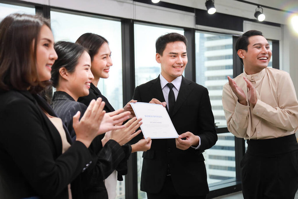 アジアの企業グループは、他の従業員が拍手している間、支店長に与えられたCEOとの会議室で一緒に祝う(偽の証明書を持つ)) - 写真・画像