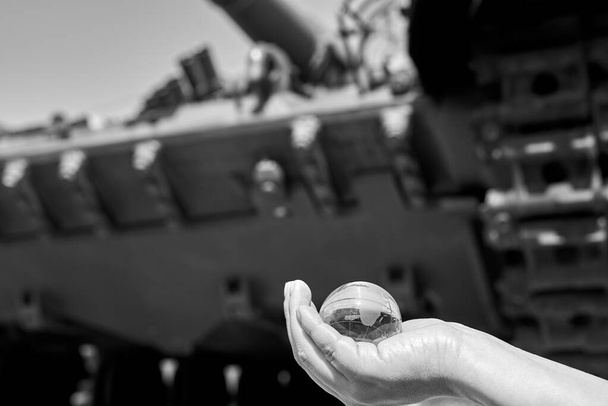 El globo de vidrio del planeta Tierra en la mano de una mujer bajo las huellas del tanque, el concepto de guerra, foto en blanco y negro. - Foto, Imagen