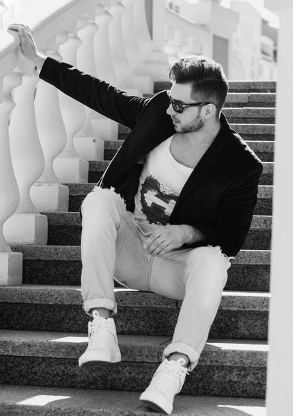 Handsome young man walk in old part city in blue jeans, black jacket, white shirt, glasses, stylish hair, good mood, beautiful fashionable boyfriend, citizen, have beauty face - Photo, Image