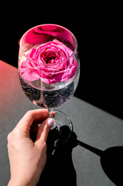 ピンクの花のペタルソンテーブルに黒で満たされたワイングラス。ミニマルな現代の静物画。休日の概念バレンタインや女性の日の背景デザイン。創造的な夏のアイデア. - 写真・画像