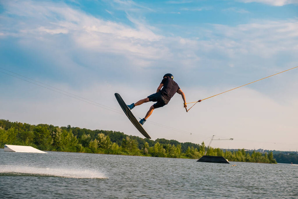 Jeune homme sautant par-dessus la surface de l'eau de la rivière sur wakeboard - Photo, image