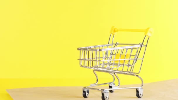 黄色の背景に空のショッピングカート、クローズアップ。ブラックフライデーショッピング&割引コンセプト - 映像、動画