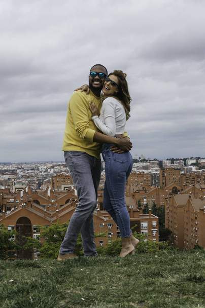 Νεαρό διαφυλετικό ζευγάρι αγκαλιάζει, γελάει και φιλιέται σε ένα πάρκο - Φωτογραφία, εικόνα