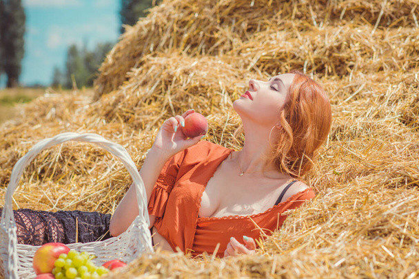 Country vintage mix stijl, vrouw met mand van fruit op het veld. Portret van een aardige dame op hooizolder - Foto, afbeelding