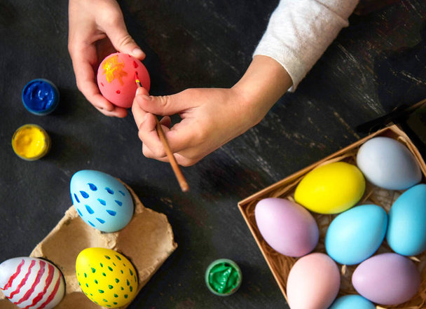 Les mains de l'enfant peignent les œufs de Pâques en différentes couleurs et motifs. - Photo, image