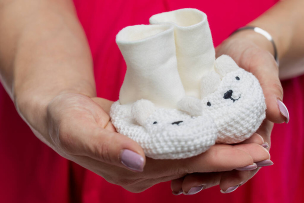 White knitted booties for a newborn in female hands. Close-up. Preparing for the birth of a baby. - Photo, Image