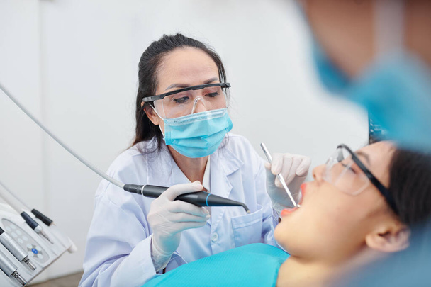 Érett tapasztalt fogorvos szemüveg és védő maszk fúrás fogak szenvedő beteg üreges - Fotó, kép