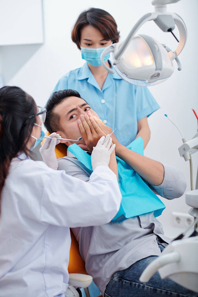 Dentysta i pielęgniarka próbują uspokoić nerwowego pacjenta, który boi się leczenia stomatologicznego - Zdjęcie, obraz