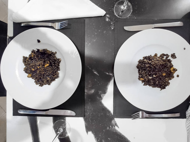 Arroz negro Spaans recept, zwarte paella met inktvis op 2 borden op een zwart-wit marmeren tafel in een Spaans Catalaans restaurant in Barcelona - Foto, afbeelding
