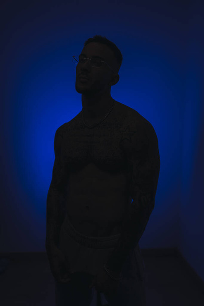 The silhouette of an athletic, muscular man in a dark room with blue light - Foto, afbeelding