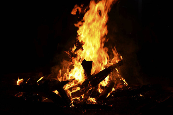 A high burning campfire in the dark night with logs and branches feeding it - Foto, imagen