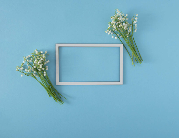 fresh white lily of the valley with white frame on baby blue pastel background. minimal natural decorative art flat lay with copy space - Foto, Bild