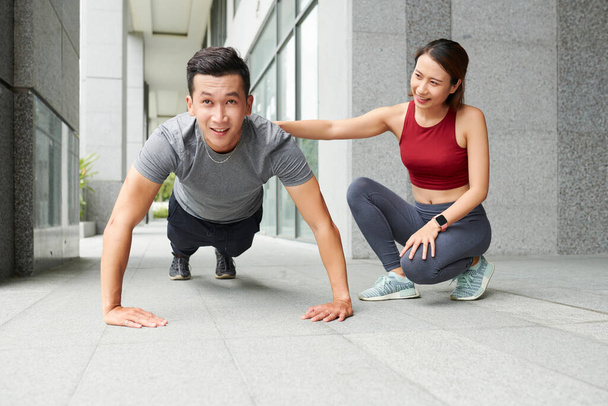 Női edző kontrolling fitt fiatal férfi csinál push-up szabadban - Fotó, kép
