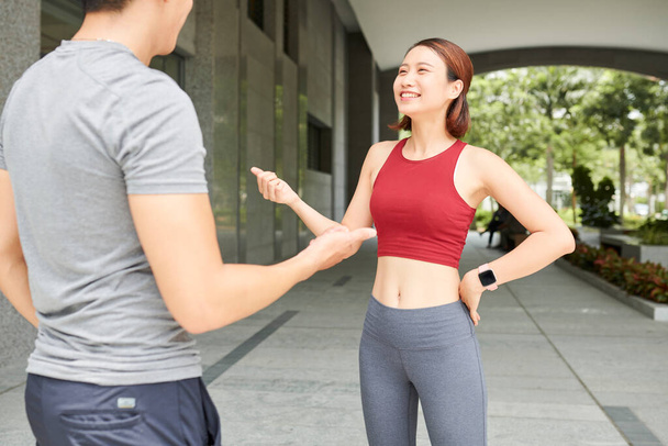 Dość uśmiechnięta młoda azjatycka sportowiec rozmawia z chłopakiem przed jogging na zewnątrz - Zdjęcie, obraz