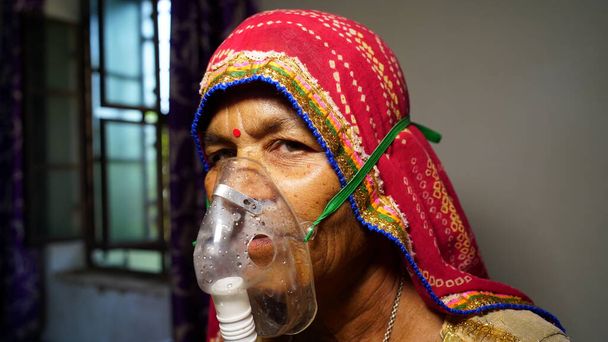 Woman suffering from Covid 19 disease. Old woman admitted in hospital and inhaling emergency oxygen with canula mask. - Photo, Image