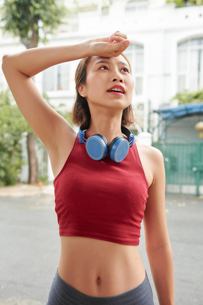 Tamelijk fit jong aziatisch sportvrouw vegen af zweet na joggen buiten in de ochtend - Foto, afbeelding