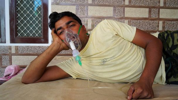 Hombre joven infectado con la enfermedad de Covid 19. Paciente inhalando oxígeno usando máscara con flujo de oxígeno líquido. - Foto, Imagen