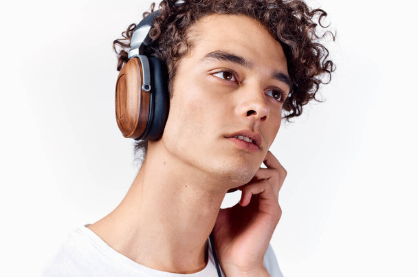 парень с вьющимися волосами в наушниках слушает музыку на светлом фоне - Фото, изображение