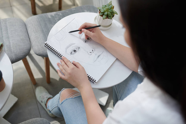 Крупным планом изображение лица талантливого студента рисования в альбоме эскизов с черными чернилами - Фото, изображение