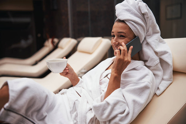 Beautiful elegant pretty business woman drinking beverage while sitting on the deck chair in spa resort hotel - Foto, imagen