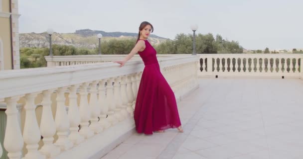 Fiatal lány piros ruhában sétál az erkélyen nappal - Felvétel, videó