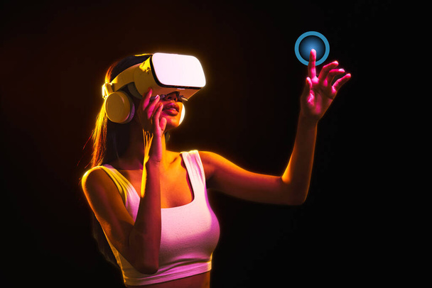 Asiatin mit VR-Headset-Brille, um virtuell auf leeren Bildschirm zu schauen und hob die Hand zum Berühren auf virtuellen Bildschirm, Digitale 3D-Simulation und Unterhaltungstechnologie zu Hause. - Foto, Bild