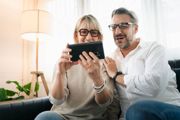 Šťastný pár staří důchodci pomocí mobilního telefonu na videokonferenční hovor s rodinou v obývacím pokoji atmosféra, Sociální distancování rodina během pandemie coronavirus. - Fotografie, Obrázek