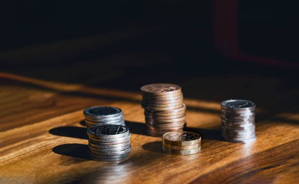 Stacks  British money sterling pound coins on wooden table, Selective focus GBP coins on the wood with shadow and light in dark room, Business and financial for money saving or investment concept - Photo, Image