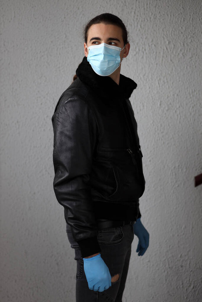 Młody atrakcyjny facet z długimi włosami noszący ochronną maskę medyczną i rękawiczki z powodu wirusa Corony. Bezpieczeństwo, ochrona, koncepcja Covid-19. - Zdjęcie, obraz