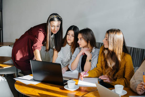 A group of young girls sit in an office at computers and discuss projects. Communication and training online. - Photo, Image