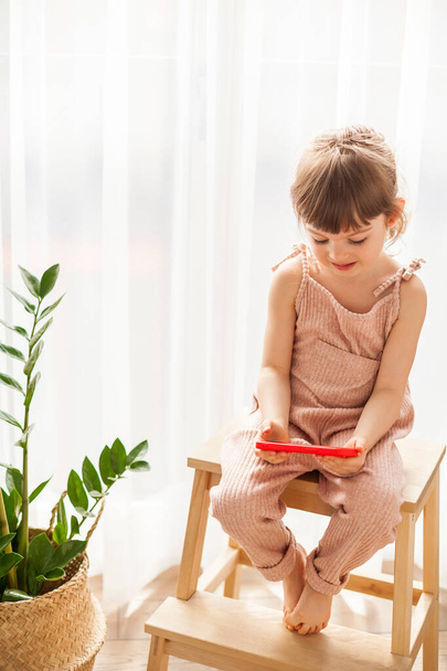 Little girl with mobile phone sitting alone. She is watching cartoons on smartphone. Digital generation and phone addiction concept. - Фото, изображение
