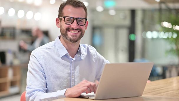 Businessman with Laptop Smiling at Camera in Office - Valokuva, kuva