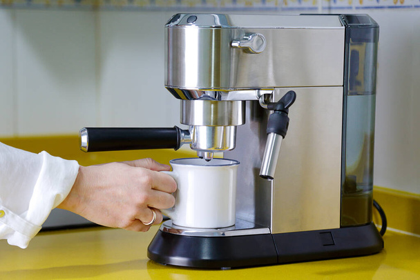 Koffiemachine die een espresso maakt en een vrouw die met haar mok wacht. Ontbijt en home equipment concept. - Foto, afbeelding