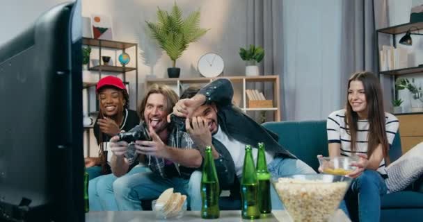 Cheerful funny emotional mixed race company sitting in front of TV set and enjoying videogames celebrating victory with giving high five and laughs - Filmmaterial, Video