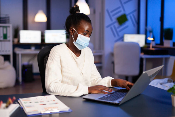 African woman with face mask reading emails late at night to respect deadline - Photo, Image