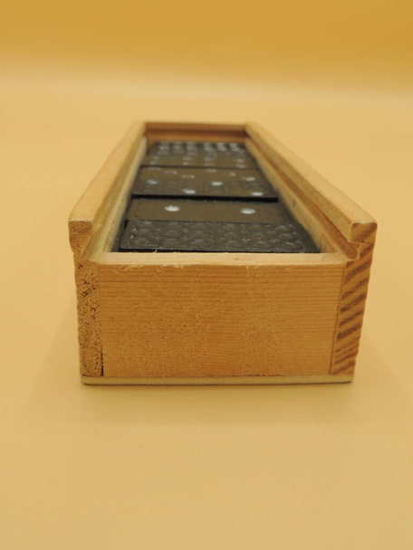 Los dominós se guardan en una caja de madera que está sobre la mesa. Fondo amarillo. Macro. Vista superior. - Foto, Imagen