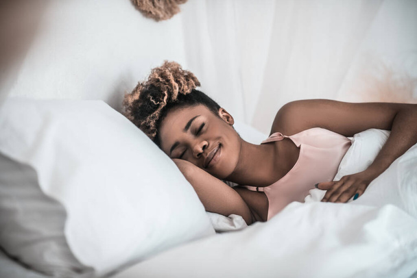 Dark skinned smiling woman napping in bed - Фото, изображение