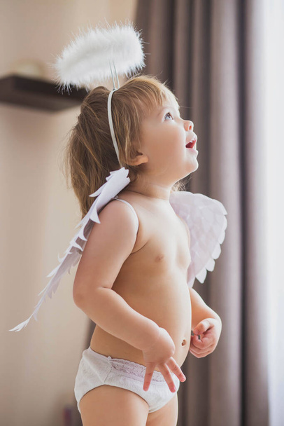 Adorable baby girl with wings and a halo looks up enthusiastically - Foto, Imagem
