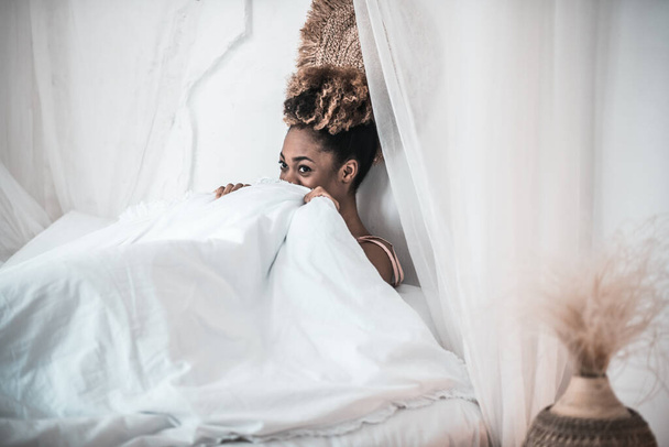 African american woman under white blanket in bed - Foto, afbeelding