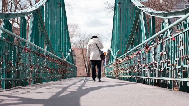 Ältere Frau mit Blindenstock in der Hand überquert grüne Brücke in der Stadt - Foto, Bild