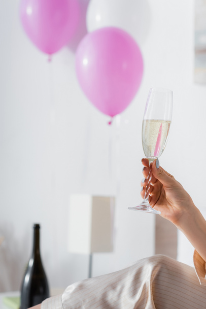 Cropped view of woman in pajama holding glass of champagne near blurred balloons  - Fotoğraf, Görsel