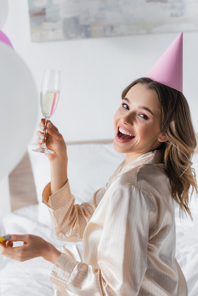 Positive woman holding glass of champagne while celebrating birthday at home  - Фото, изображение
