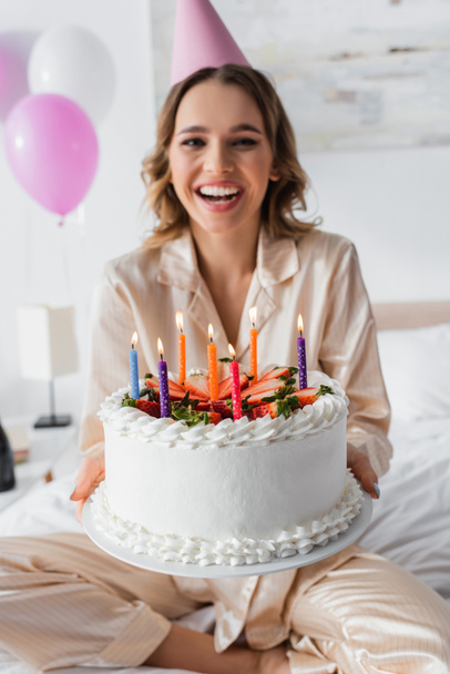 Birthday cake with candles in hands of blurred woman on bed  - Foto, imagen