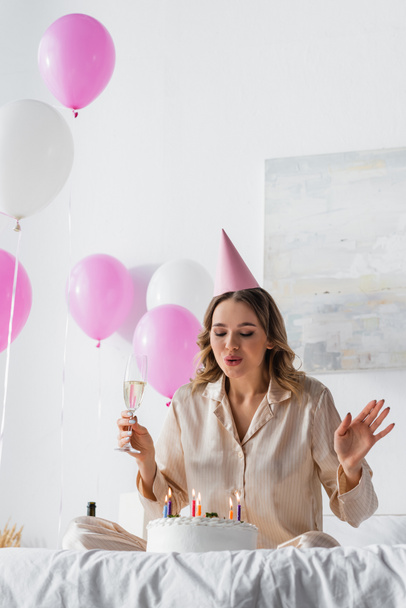Donna con champagne che spegne candele sulla torta di compleanno sul letto  - Foto, immagini