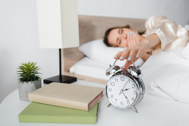Blurred woman holding alarm clock near books in bedroom  - Foto, afbeelding