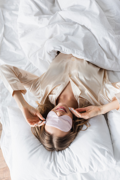 Vista dall'alto della donna sorridente in maschera addormentata sdraiata sul letto  - Foto, immagini