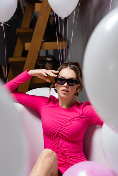 Stylish woman in sunglasses sitting in bathtub near balloons during party  - 写真・画像