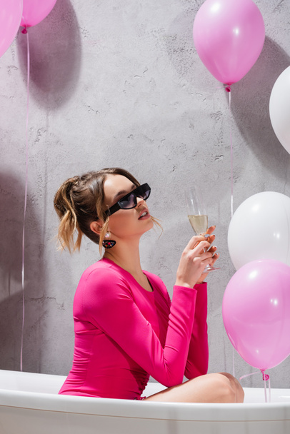 Стильна жінка тримає келих шампанського у ванній біля кульок
  - Фото, зображення